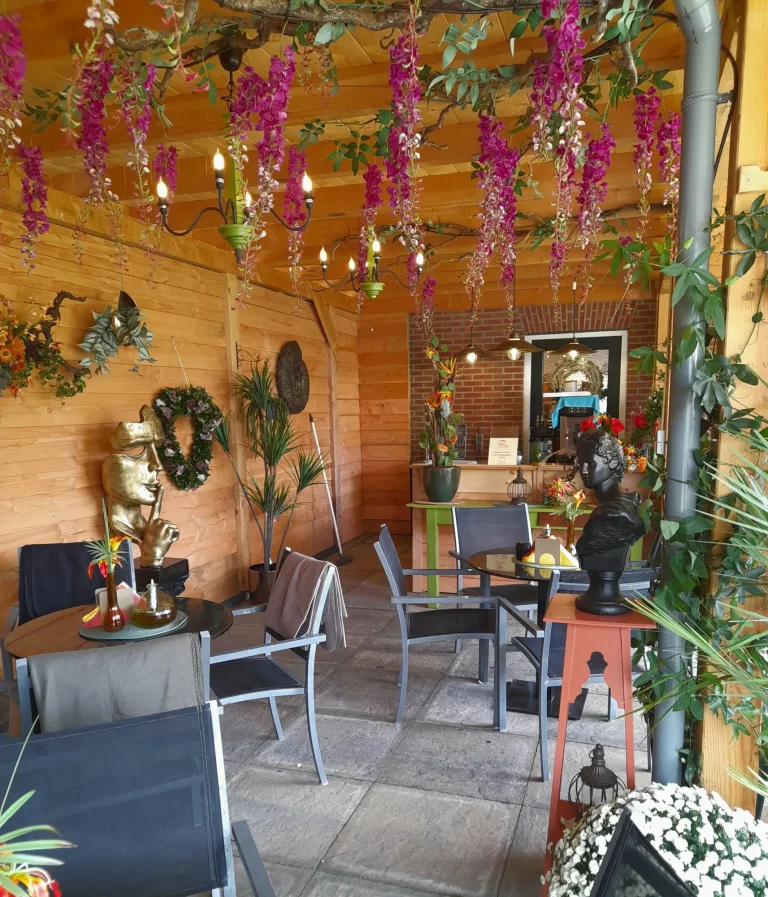 Gezellige zithoek onder hangende bloemen op het terras – Bloem en Atelier Floriante