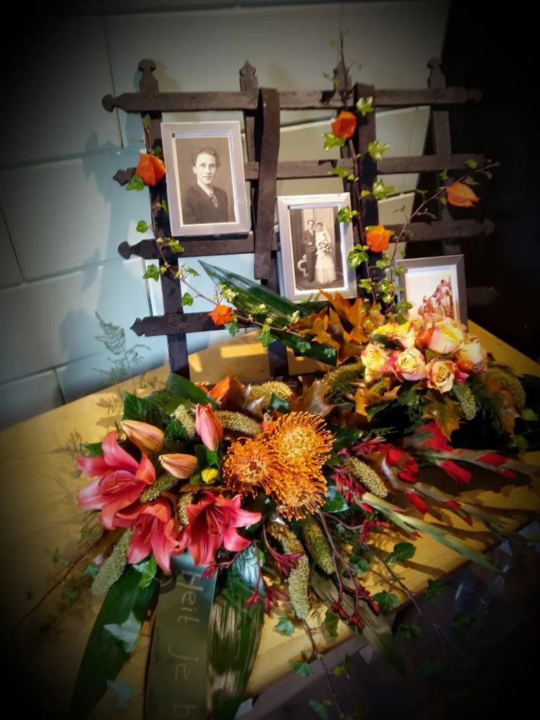 Rouwbloemwerk in oranjetinten bij foto's van de overledene – Bloem en Atelier Floriante